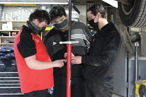 作为职业教育的一部分，绿烟囱学校的学生在当地企业工作. 这张照片显示了布鲁斯特壳牌公司一辆汽车下的3个人, 其中两人是绿烟囱的学生.
