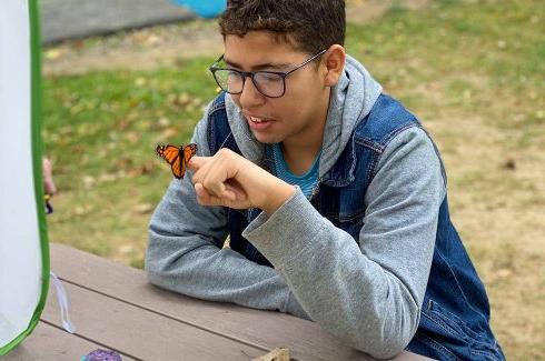 绿烟囱的学生们坐在户外的一张桌子旁，看着栖息在他手指上的蝴蝶.