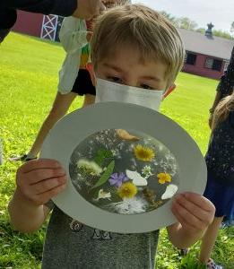 学龄前儿童拿着一个由纸板圈组成的项目, 一个半透明的接触纸中心，上面放着花和叶子.